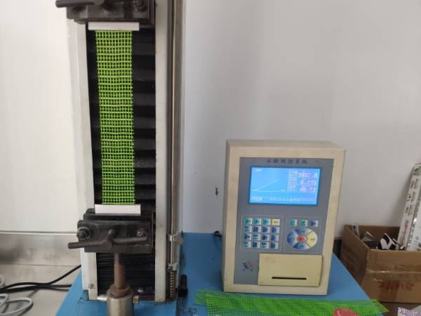 The machine is conducting fiberglass mesh tensile strength test.