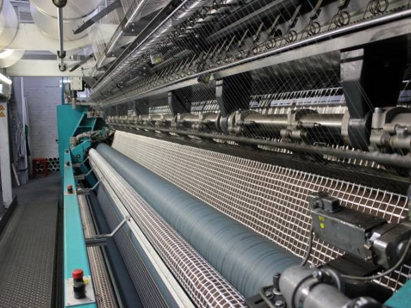 The machine is weaving fiberglass yarns into woven fabric.